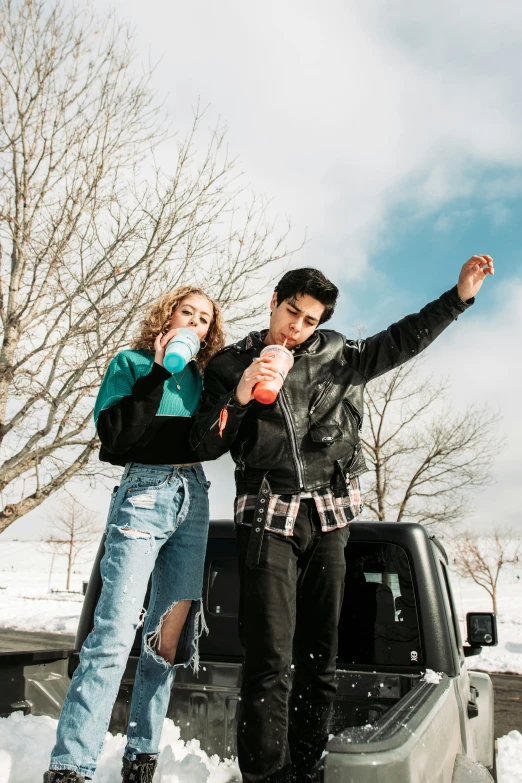 a man and woman with snow on the ground next to a truck