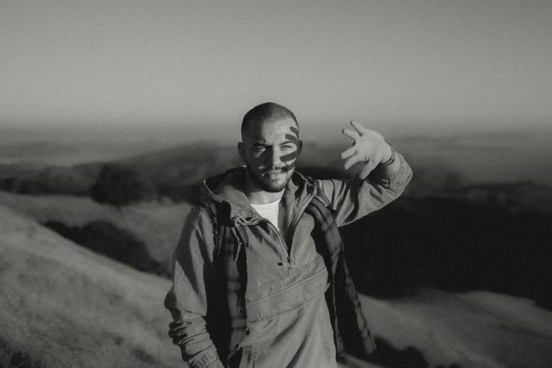 man wearing a hoodie standing on a hill with his arms stretched wide