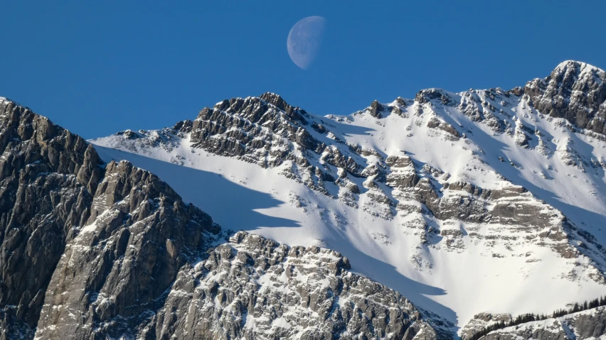 a full moon is visible above a mountain range