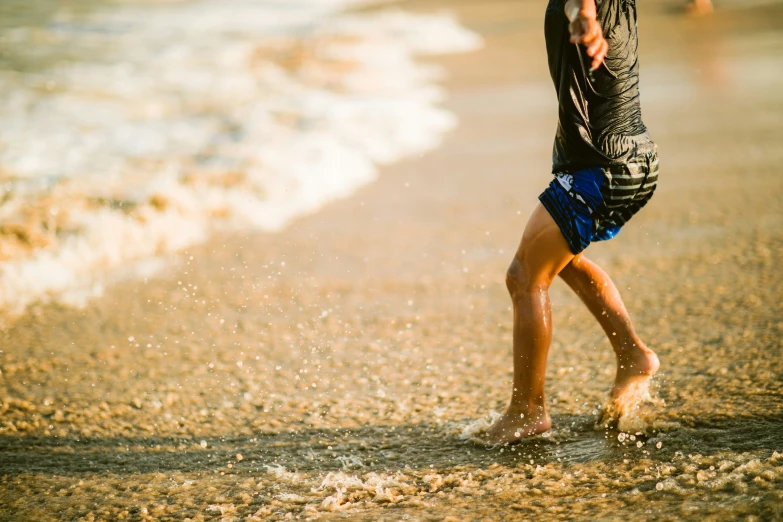 a man with blue shorts and sandals walking along the beach