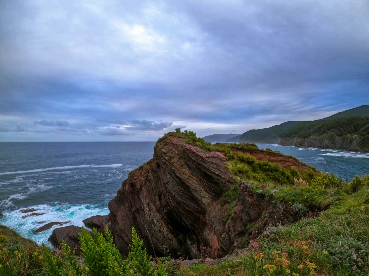 the view from the top of a large cliff with an ocean and mountains in the background