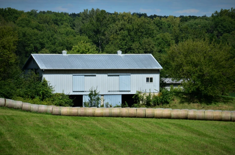 an abandoned white barn in a field surrounded by trees