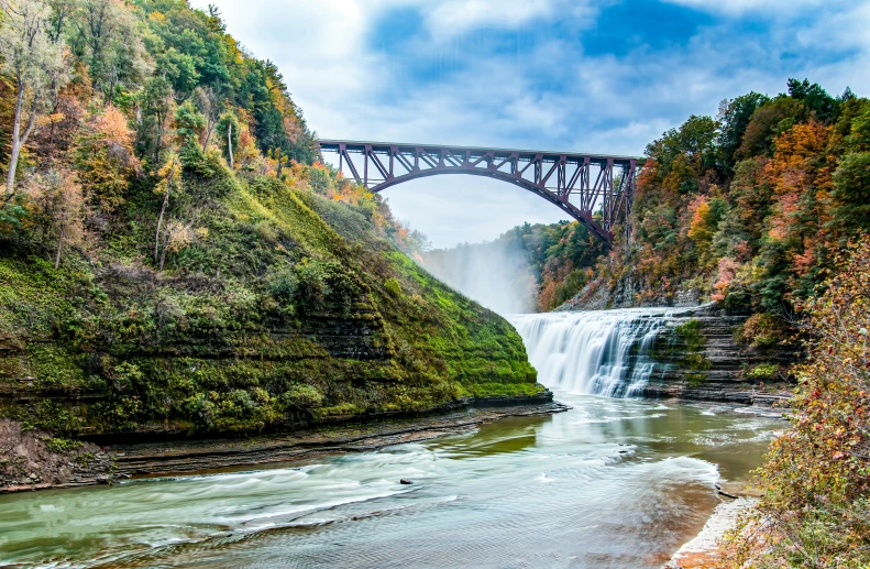 a waterfall and a bridge above it that has water flowing