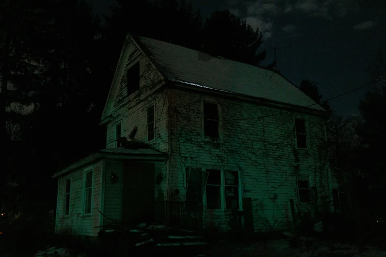 a dark abandoned farmhouse building sitting in a field at night