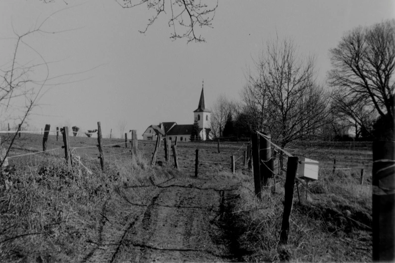 a barn and tree line the land behind a barbed fence