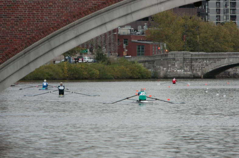 three people rowing in a boat under a bridge