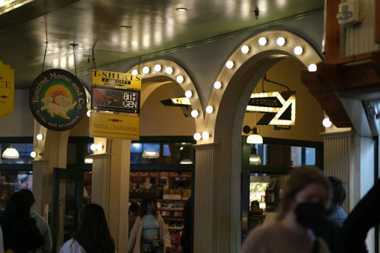 people walk inside a store with marquees above the arches