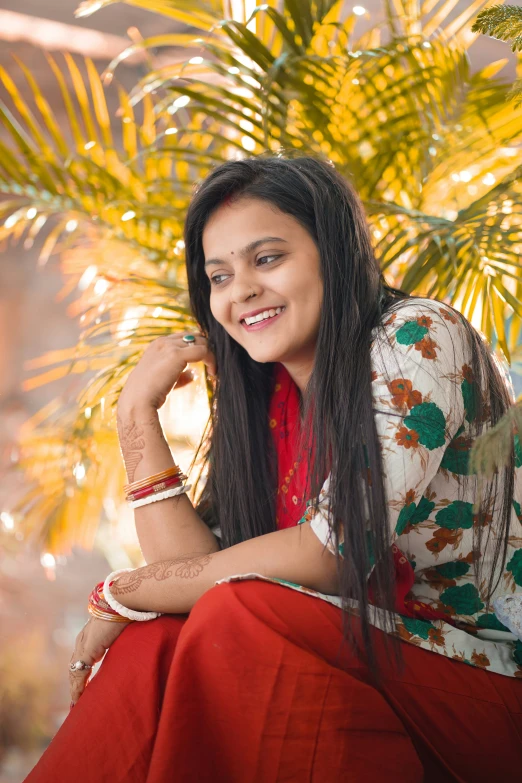 a woman with long dark hair and an ethnic print shirt sitting on the ground