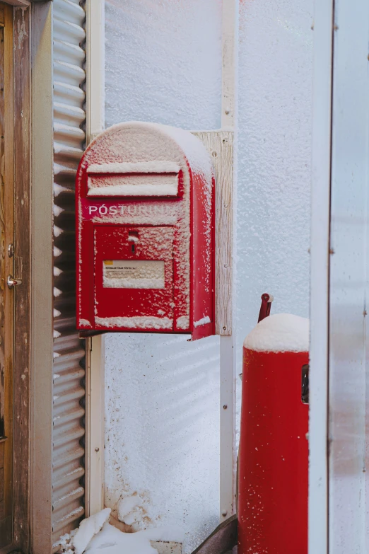 a red mail box sitting next to a snow covered building