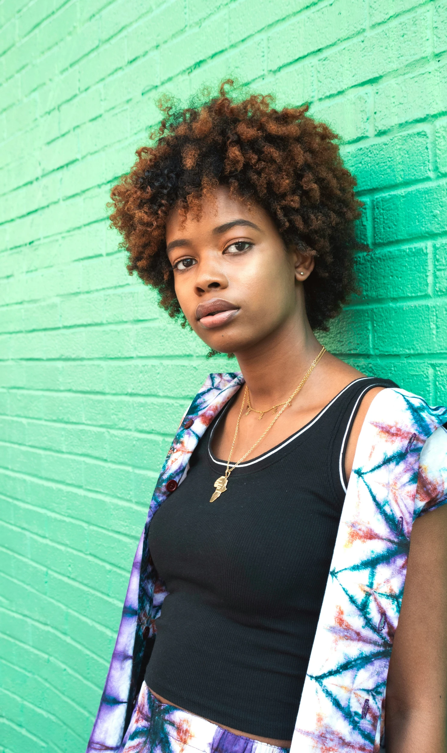 a woman stands against a green wall wearing an afro style wig