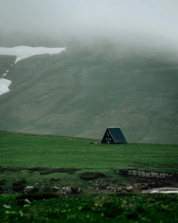 the small cabin is on the edge of a lush green hill