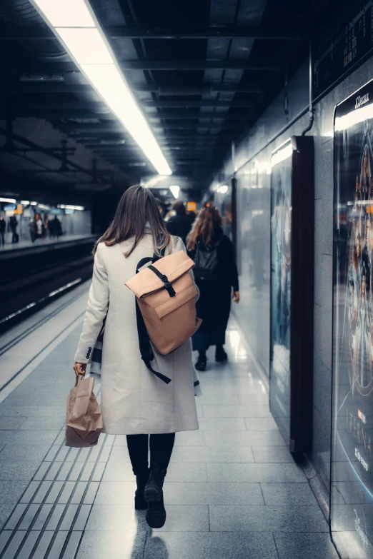 a woman is carrying a backpack and walking down a subway