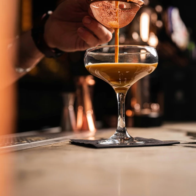 someone pouring liquid into a wine glass to make a cocktail