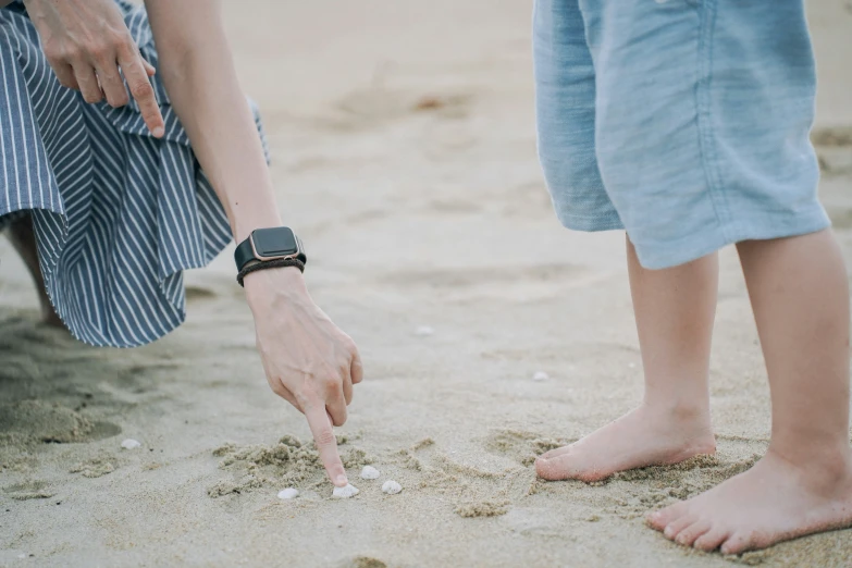 an adult pointing at a child who is standing in sand