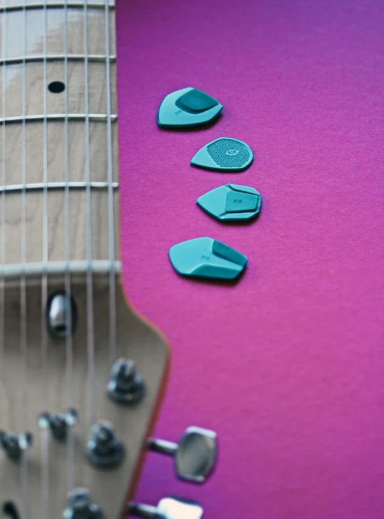 three guitar picks laying out on a pink guitar body