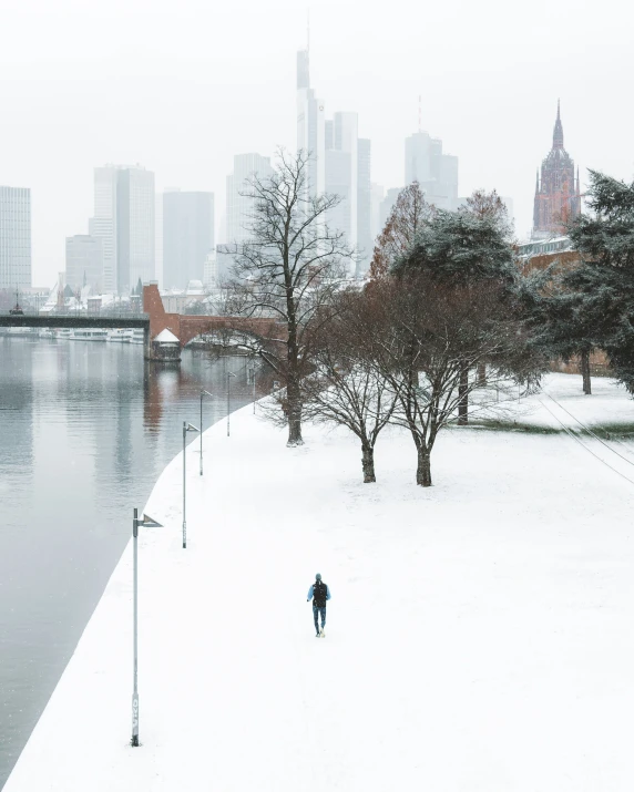 a man walking across a snow covered field next to a river