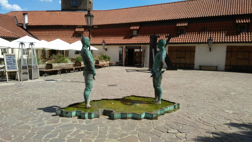 the green metal statues are on the brick walkway