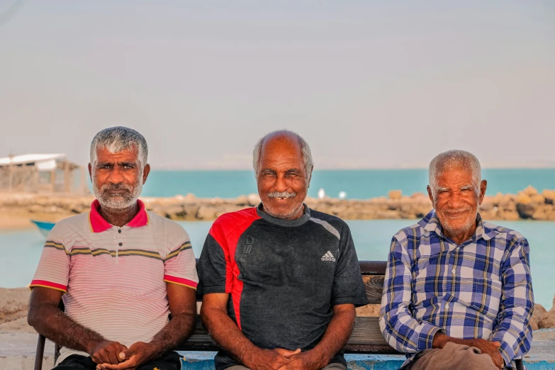 three men are sitting on a wooden bench