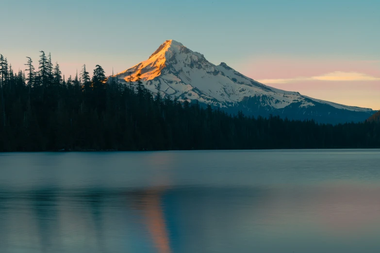 the sun setting at a lake and the snow capped mountain reflected in water