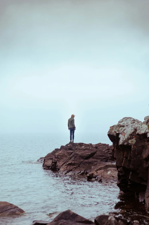 man standing on rock formation with open ocean and low sky