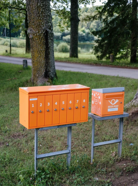 two rows of orange and grey mail boxes in grass next to tree