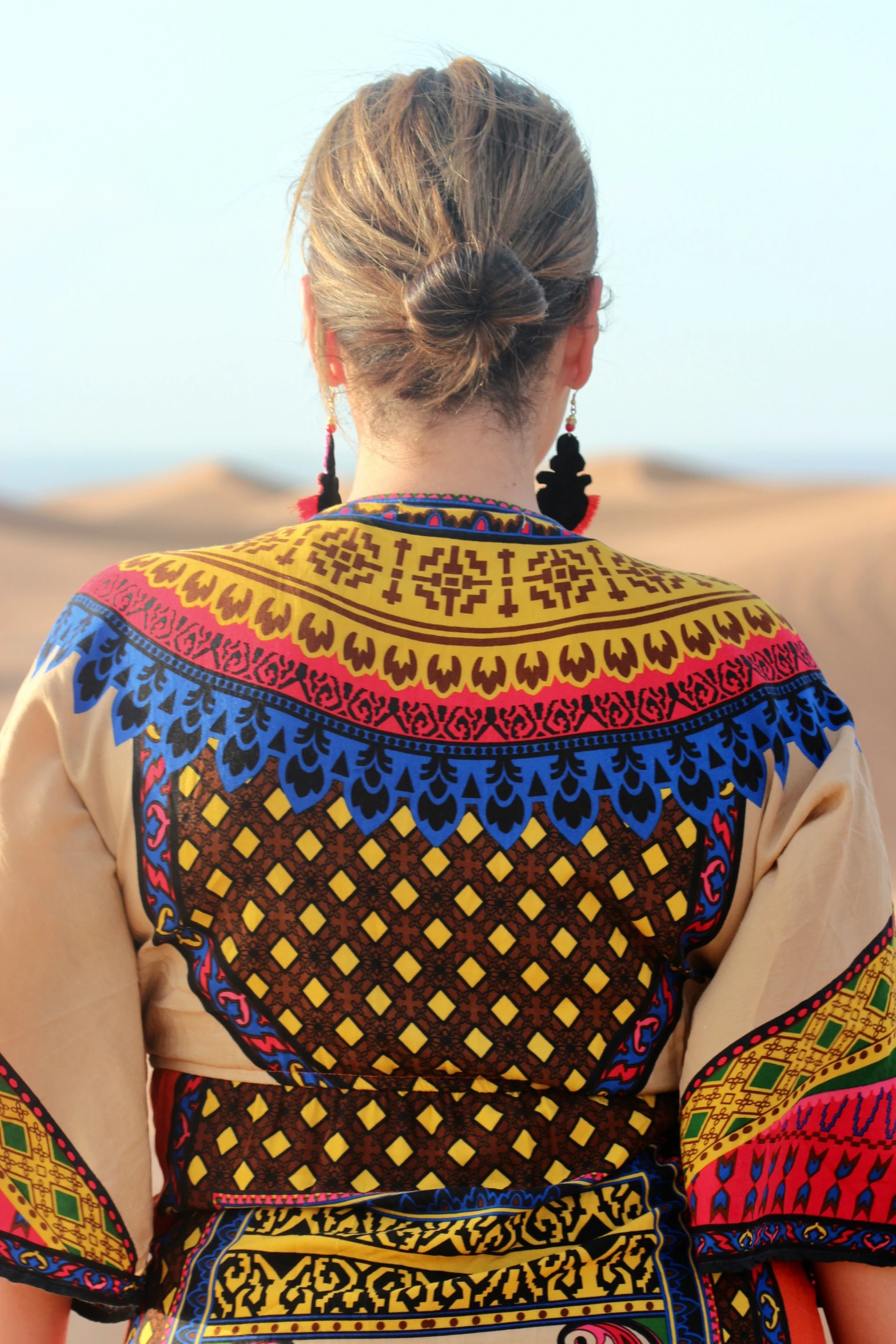 a woman wearing colorfully designed clothing standing in the desert