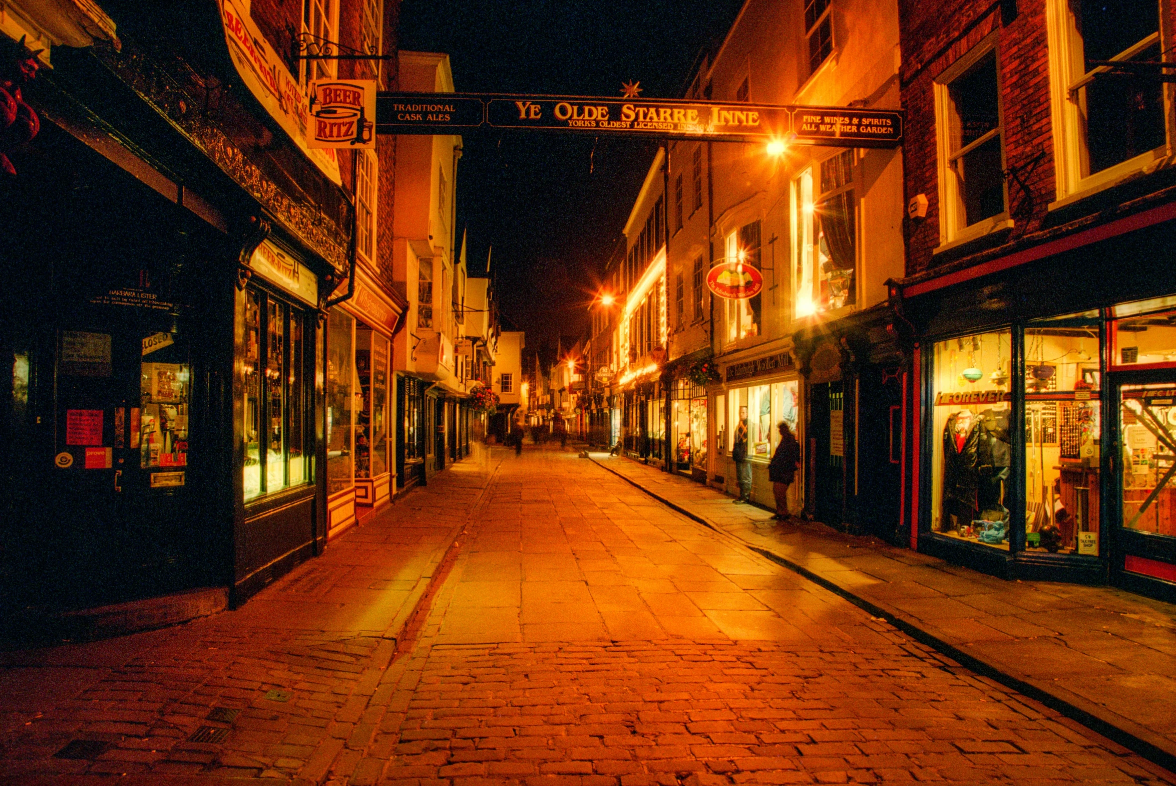 a narrow city street lined with shops at night