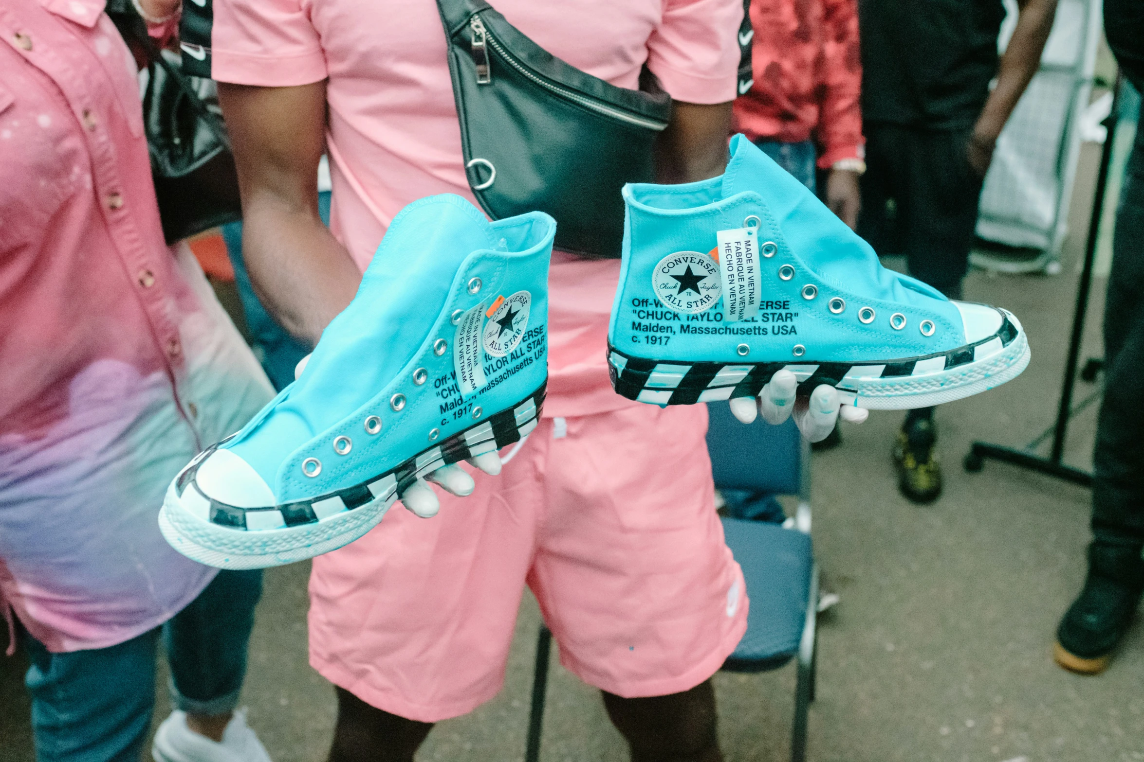 man with pink and blue outfit carrying a handbag and pair of shoes