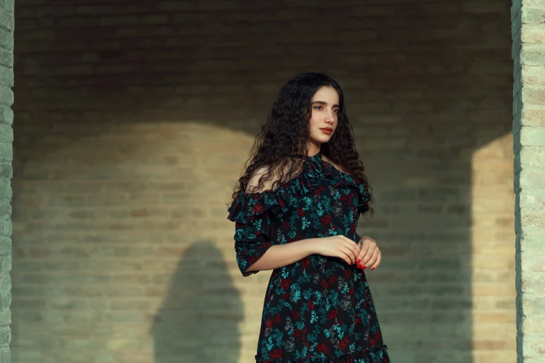 a woman in an off shoulder dress leaning against a brick wall