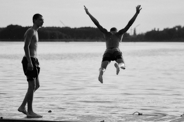 two men are watching a young man jump off of a dock