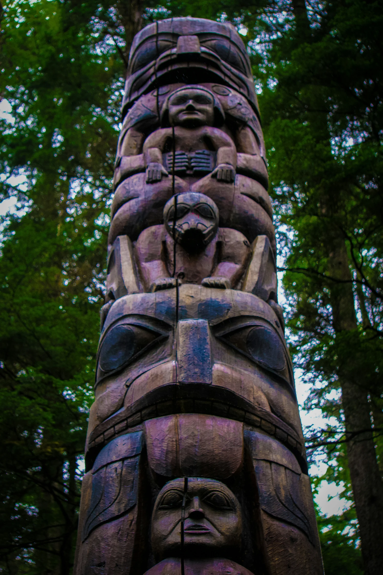 a wooden carved column surrounded by tall trees