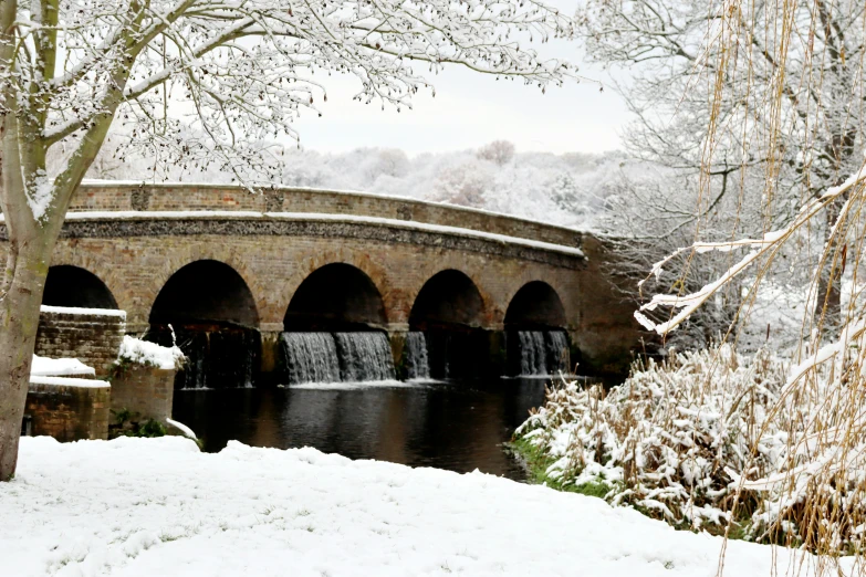 a stone bridge with a water fountain in the middle surrounded by snow