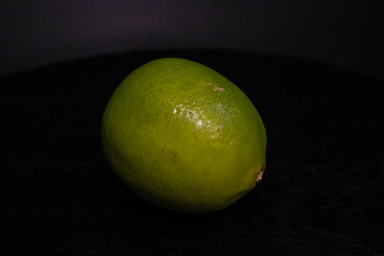 a bright green piece of fruit sitting on a dark surface