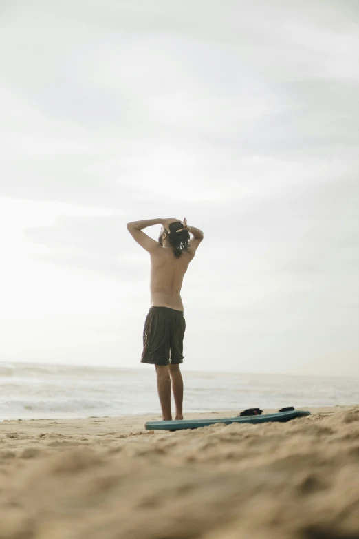 man wearing swimming trunks standing on a surfboard in the sand