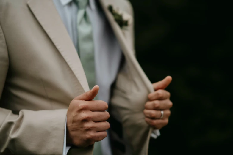 a man wearing a beige suit and green bow tie holding his thumbs up