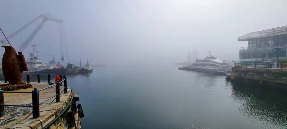 a harbor with large boats in the fog and people standing on the dock