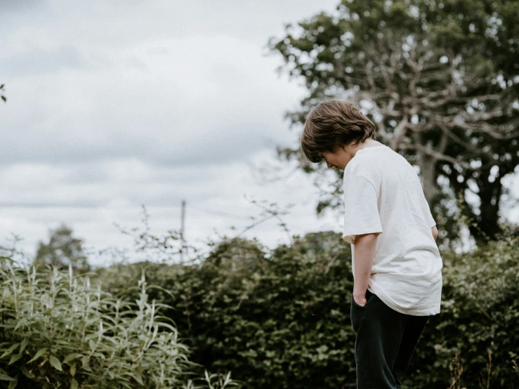 boy with white shirt and black shoes on skateboard near bushes