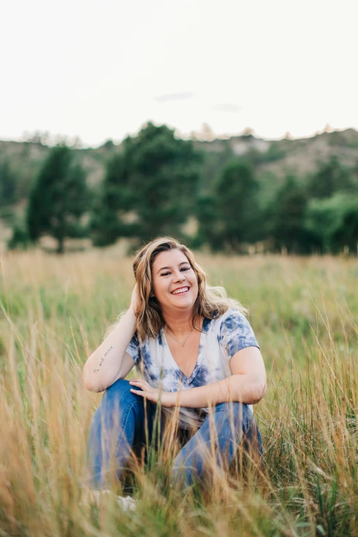 a woman sitting in a field of tall grass smiling at the camera