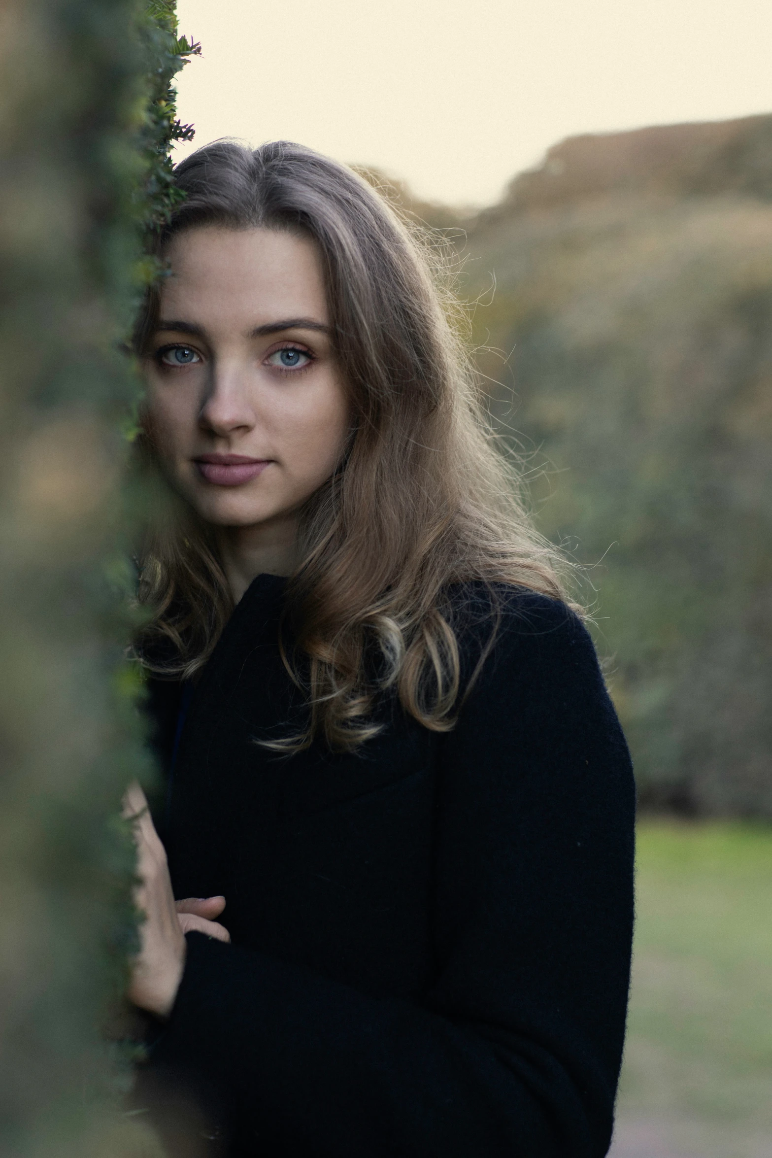 a woman is standing behind some bushes