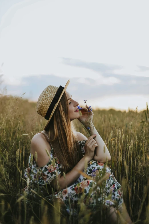 a woman with a straw hat and dress sitting in a field