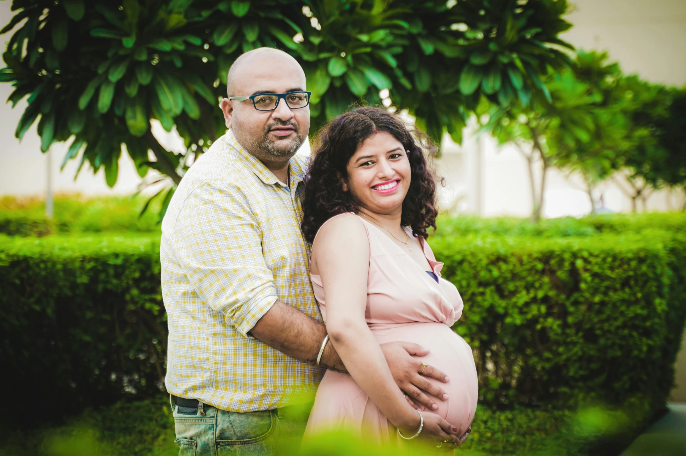 a pregnant woman and man are standing in front of a tree