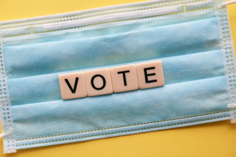 word vote spelled with cubes in blocks on blue cloth and protective mask