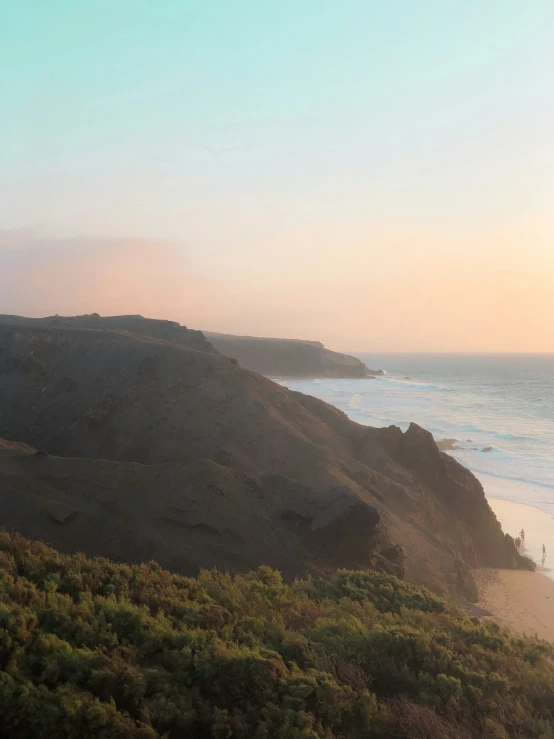 two surfers are walking on the beach at sunset