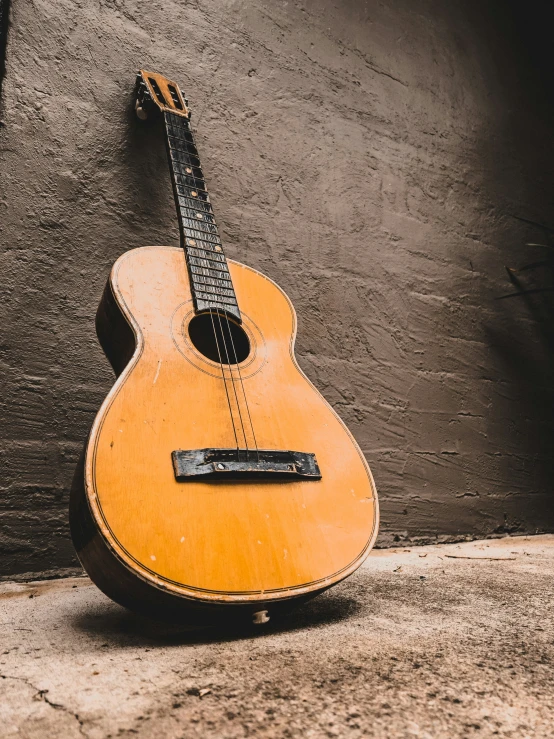 an old wooden guitar sitting against a grey wall