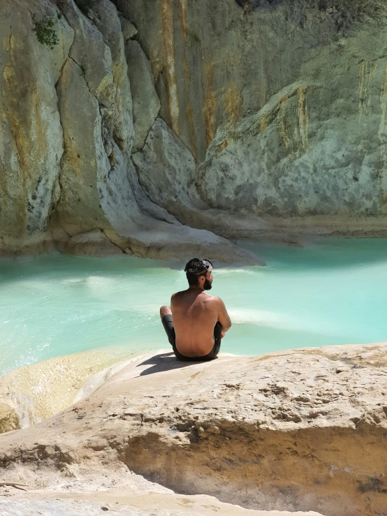 a person sitting on a rock next to a blue pool