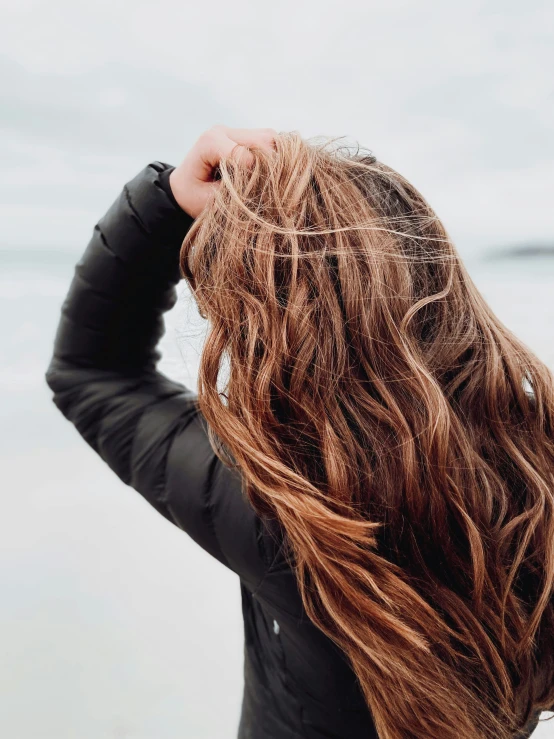 a woman standing by the ocean with her hair blowing back