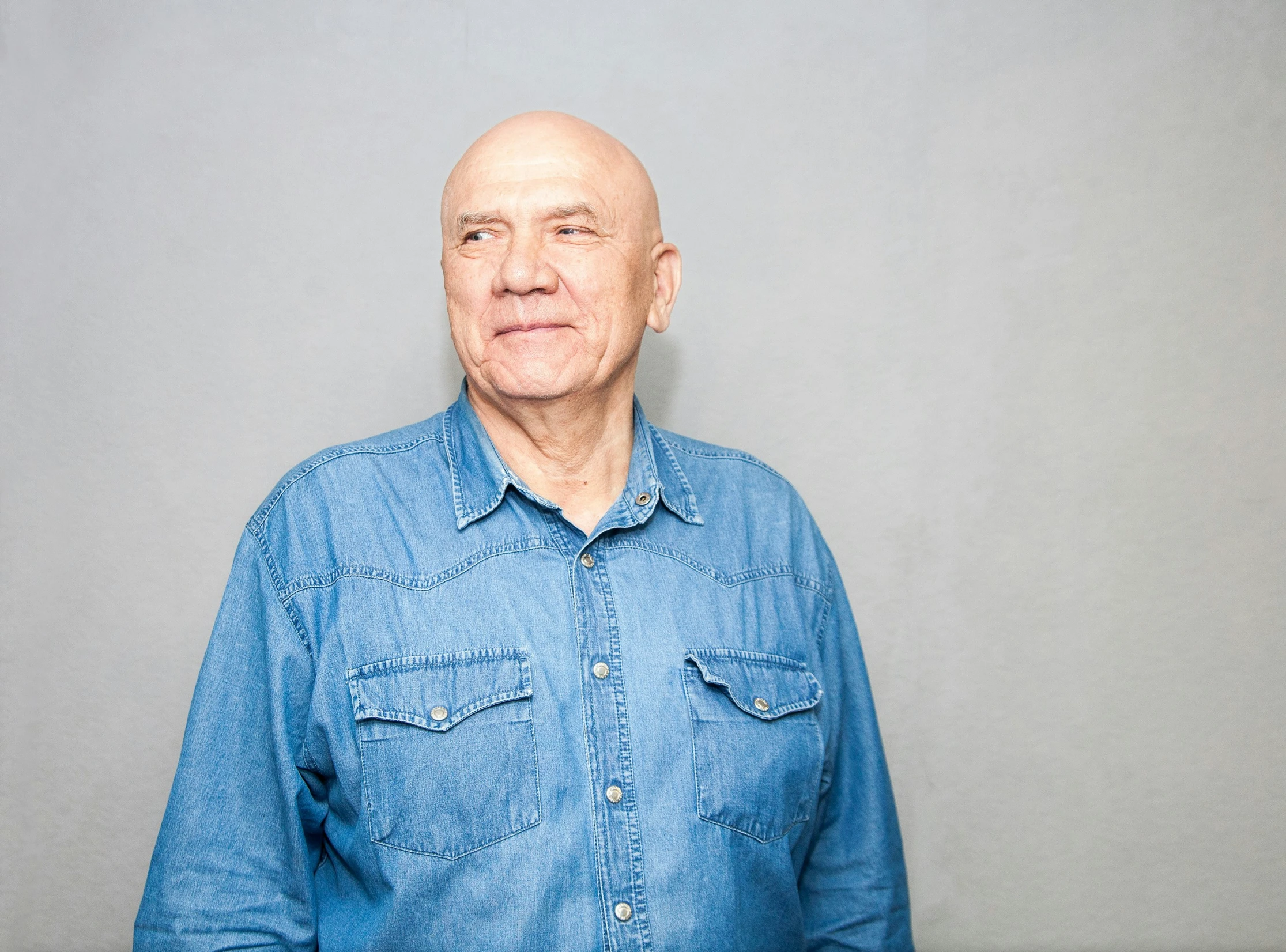 an older man in a denim shirt poses for a portrait