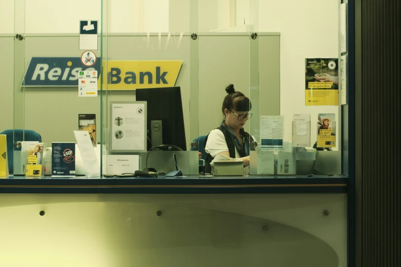 woman sitting behind the counter at a bank with a lot of items on it