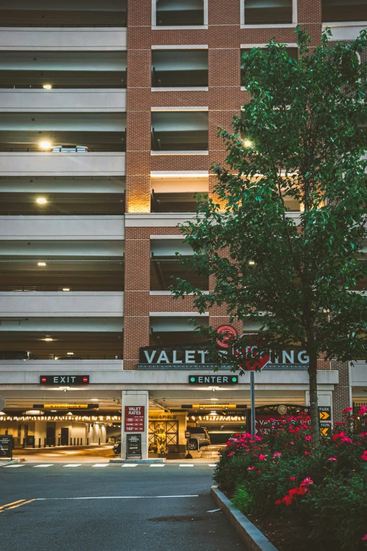 a tall brick building next to a street in front of flowers and trees