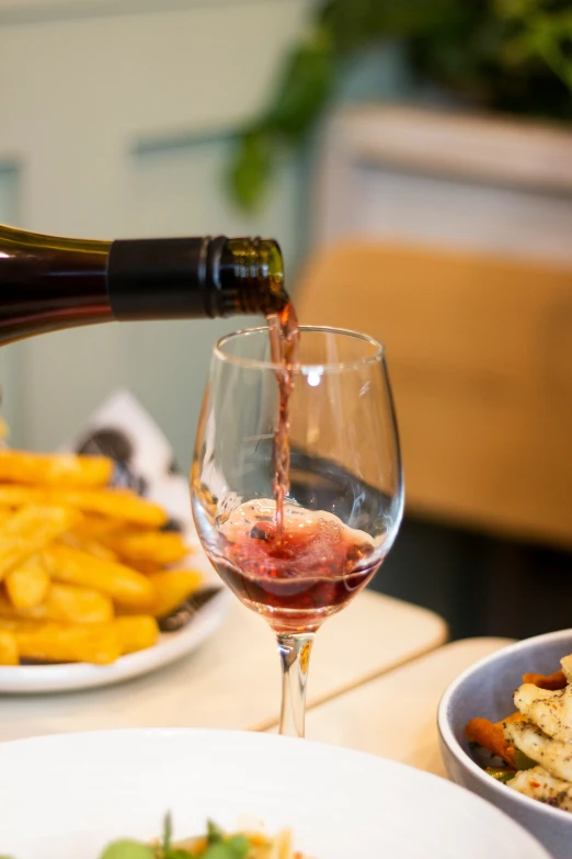 someone pouring wine into a glass and some food on the table